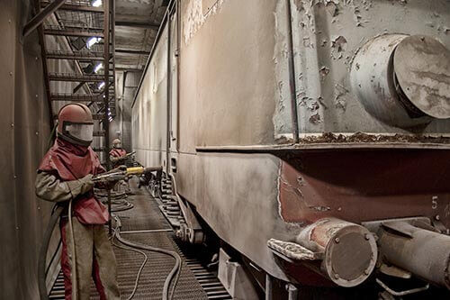 Un technicien décape une locomotive ancienne